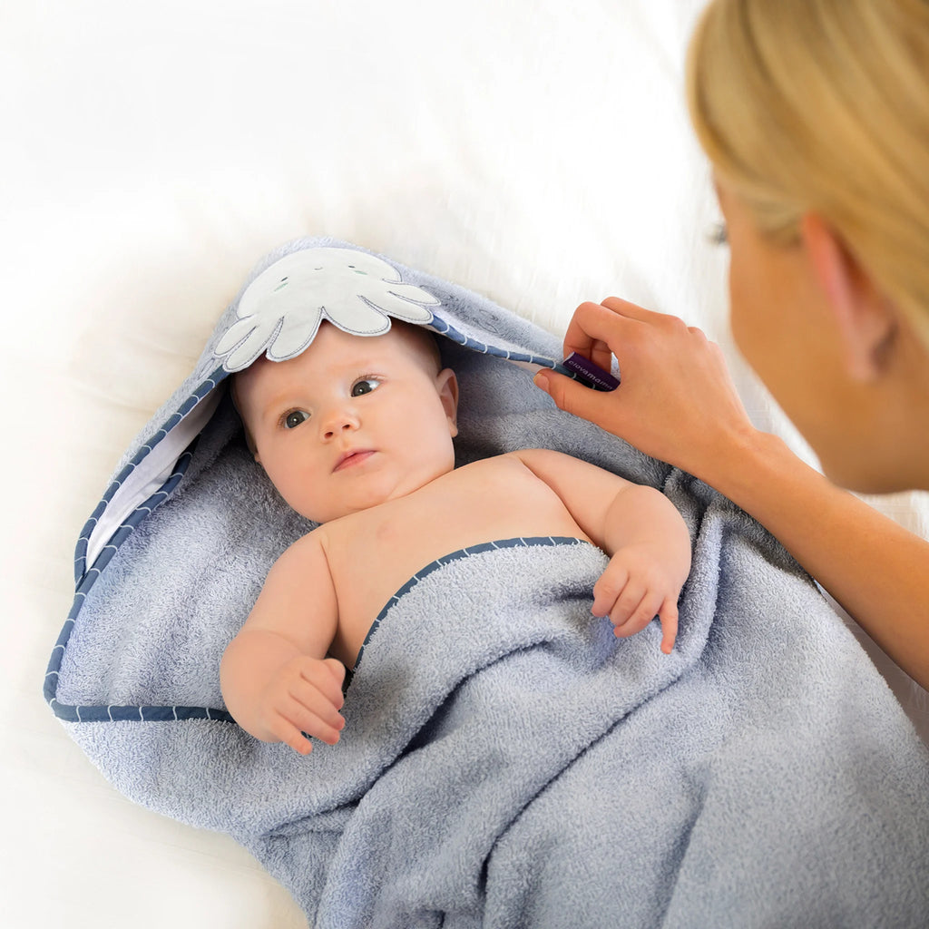 Baby wrapped in a blue hooded towel with mum assisting, on a white background