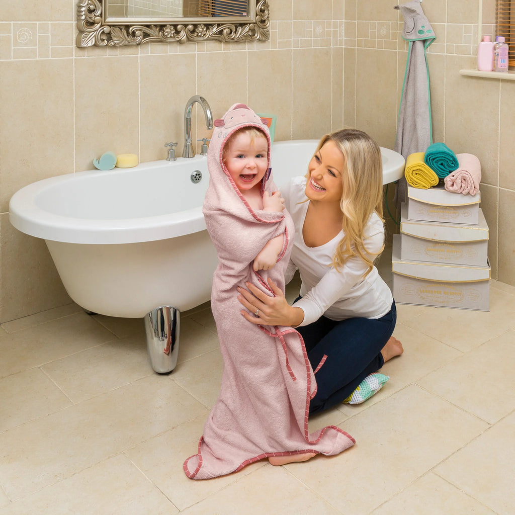 Woman holding a child wrapped in a pink towel in a bathroom.