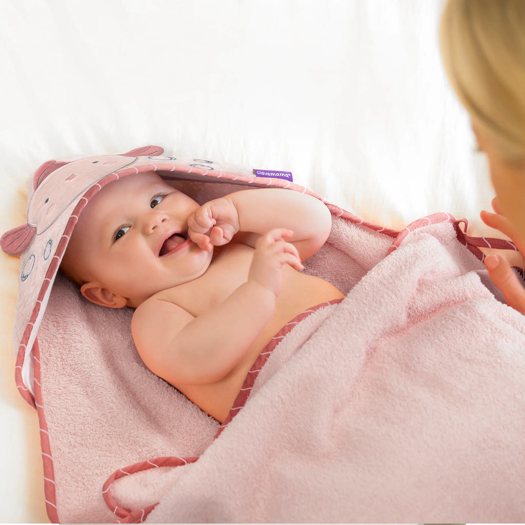 Baby lying on a pink towel with a hood, looking at a person off-camera.