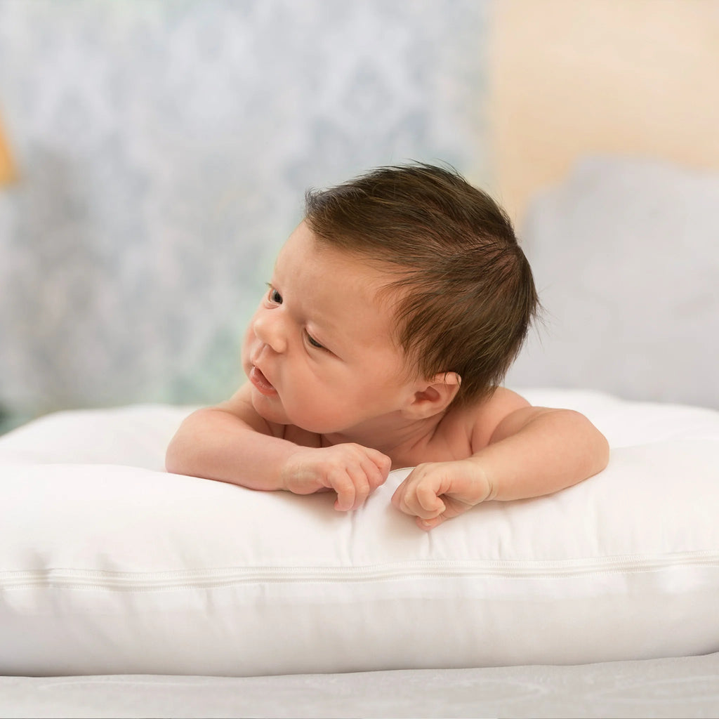 Newborn baby during tummy time on ClevaFoam Baby Pod, ergonomic white baby lounger supporting head, neck and body development, safe pod bed for comfort and anti-flat head prevention.