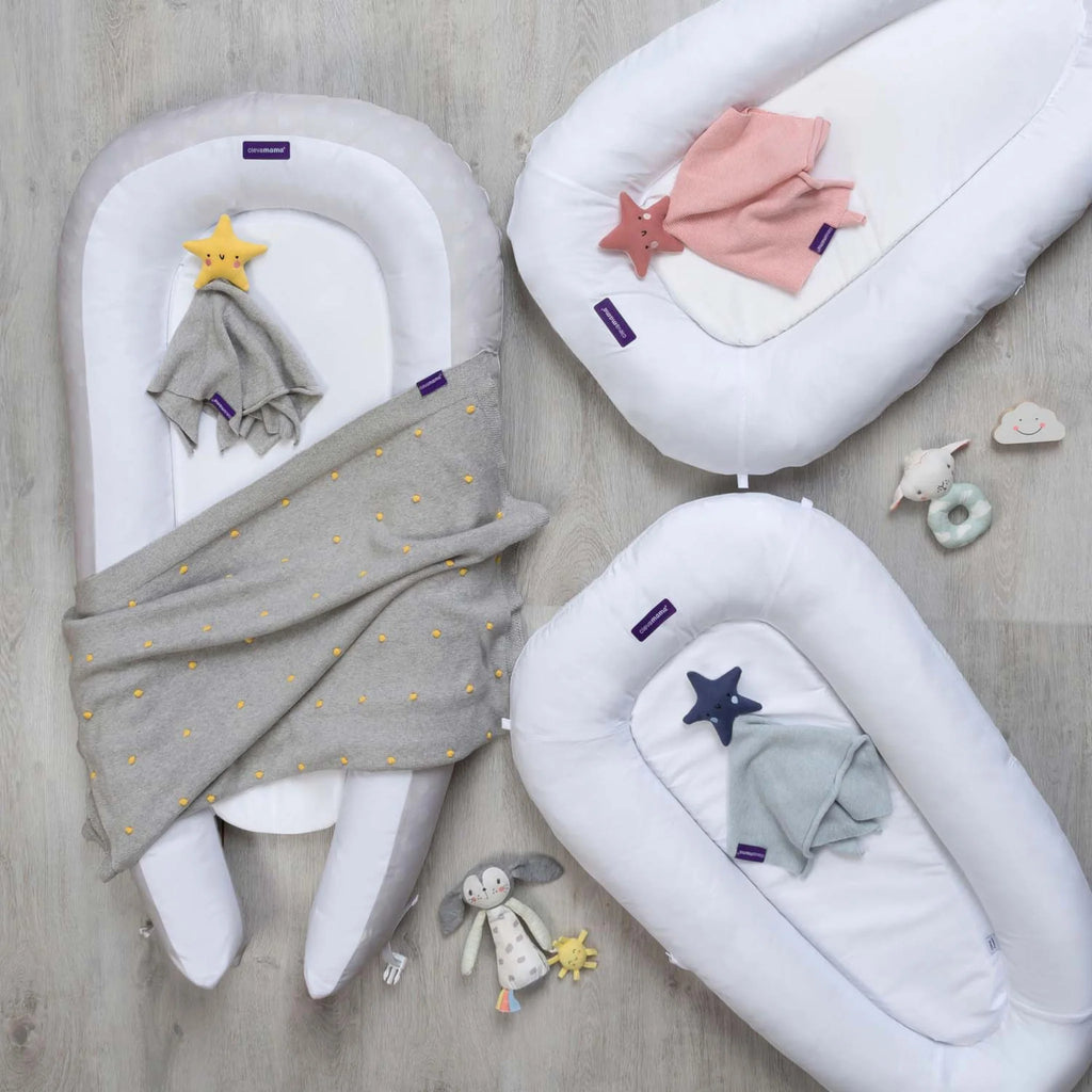 Set of ClevaFoam Baby Pods in white with soft padded sides, displayed with blankets and toys, ergonomic newborn lounger and portable baby pod bed for safe sleep, play and anti-flat head support.