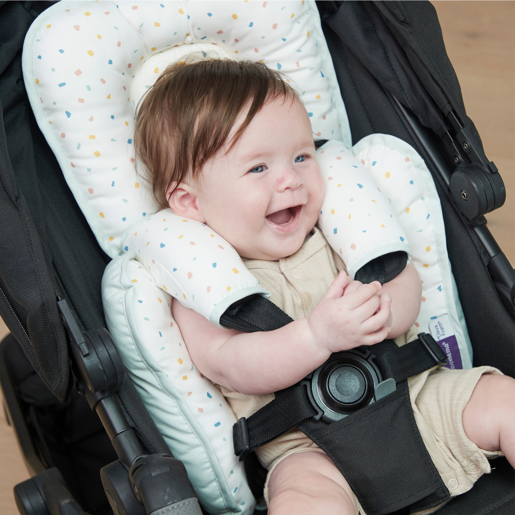 Smiling baby seated in stroller with padded car seat insert cushion – soft cotton newborn support with colorful confetti print for comfort and secure fit.
