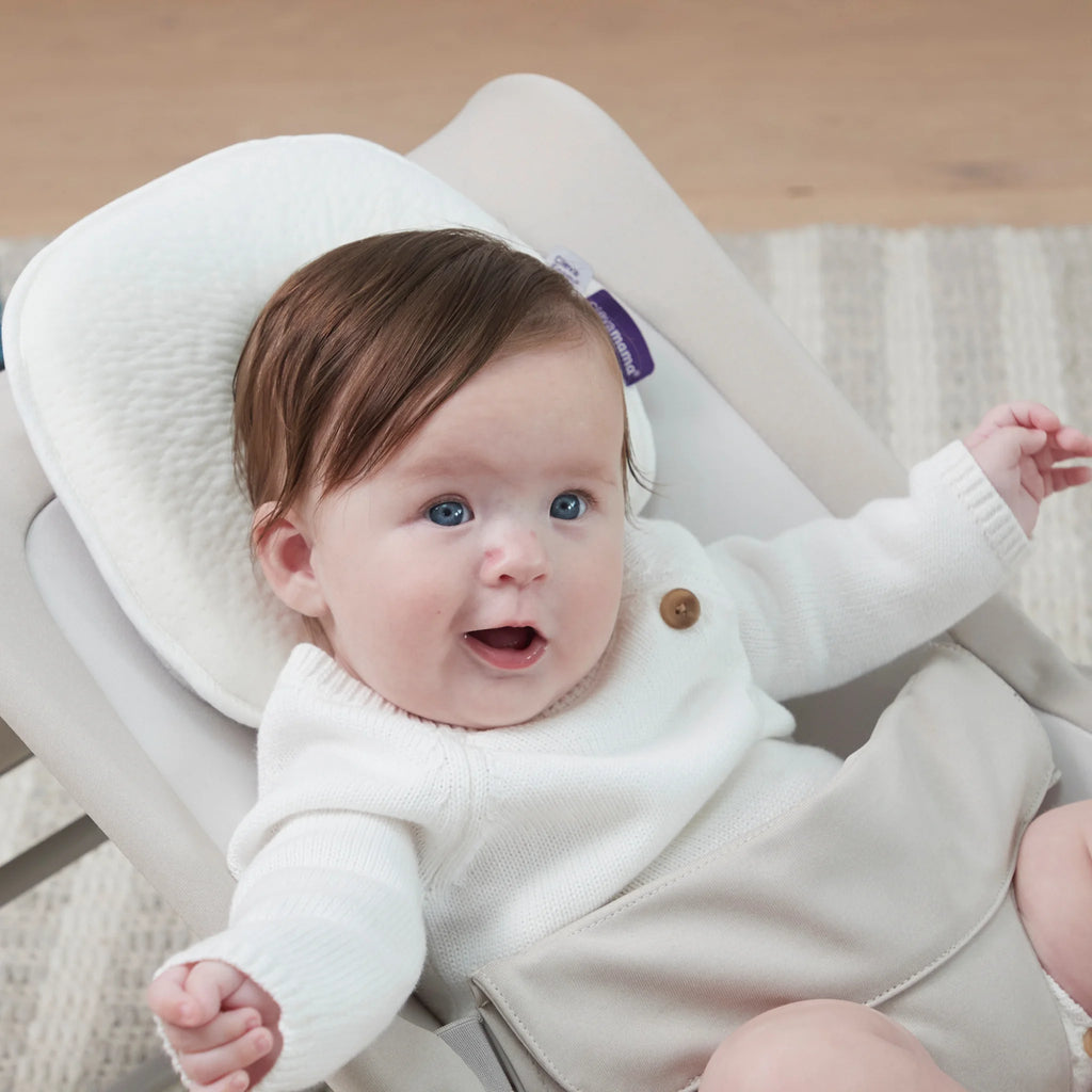 Baby in a white outfit sitting in a baby bouncer with a neutral background and ClevaMama Infant Pillow