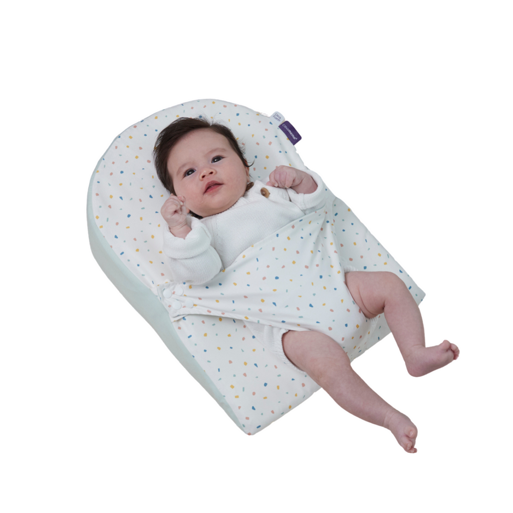 Baby lying on newborn wedge pillow with adjustable swaddle wrap breathable cotton sleep positioner in colorful confetti dot print for comfort and safe support."