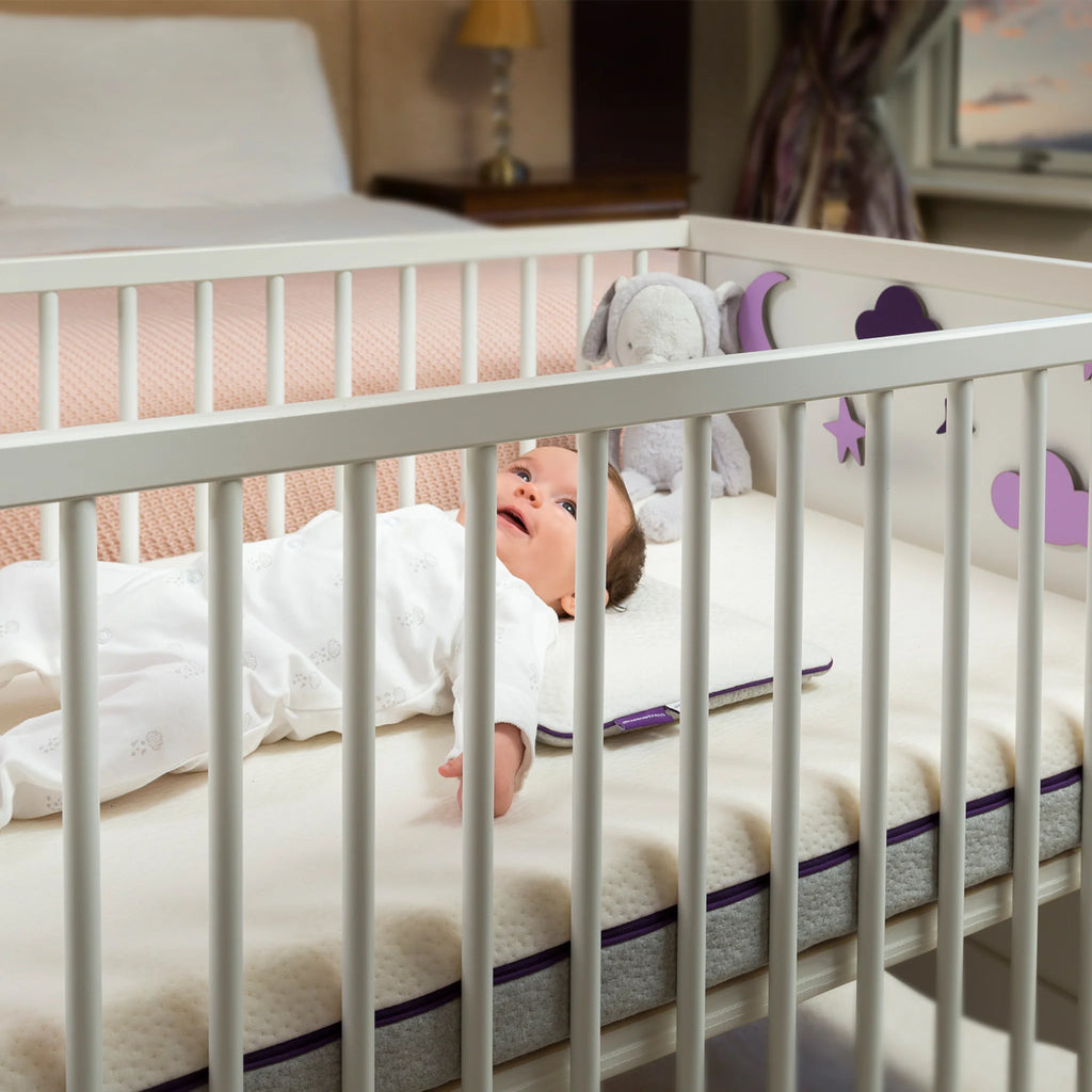 Baby lying safely on breathable hypoallergenic cot mattress in white crib – premium foam crib mattress for infant comfort, support and safe sleep