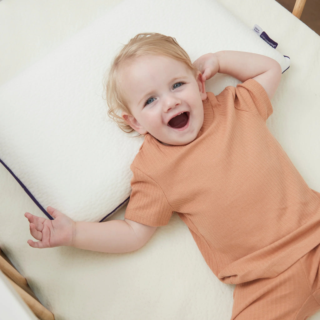 Baby in a peach outfit lying on a ClevaFoam Toddler pillow and premium support mattress.