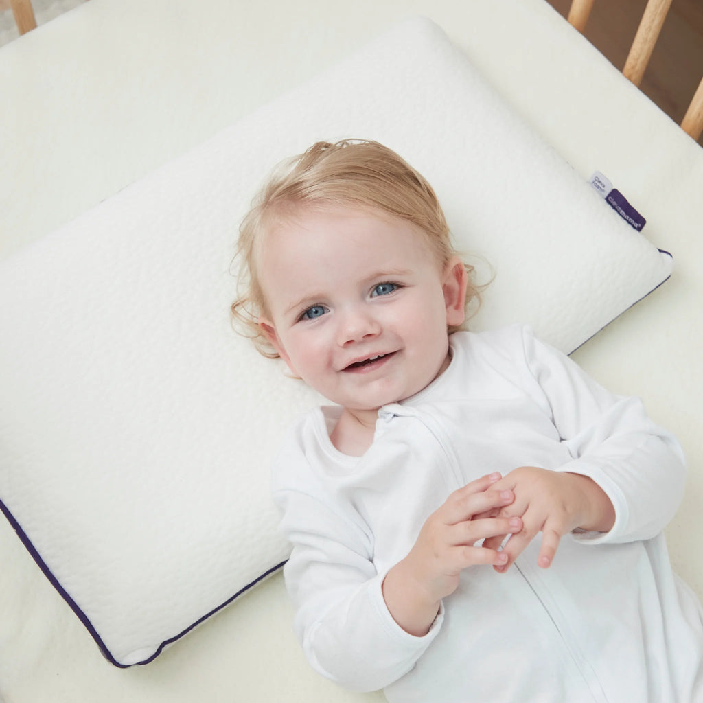 Child smiling lying down in cot on toddler pillow and ClevaFoam Premium Support Mattress.