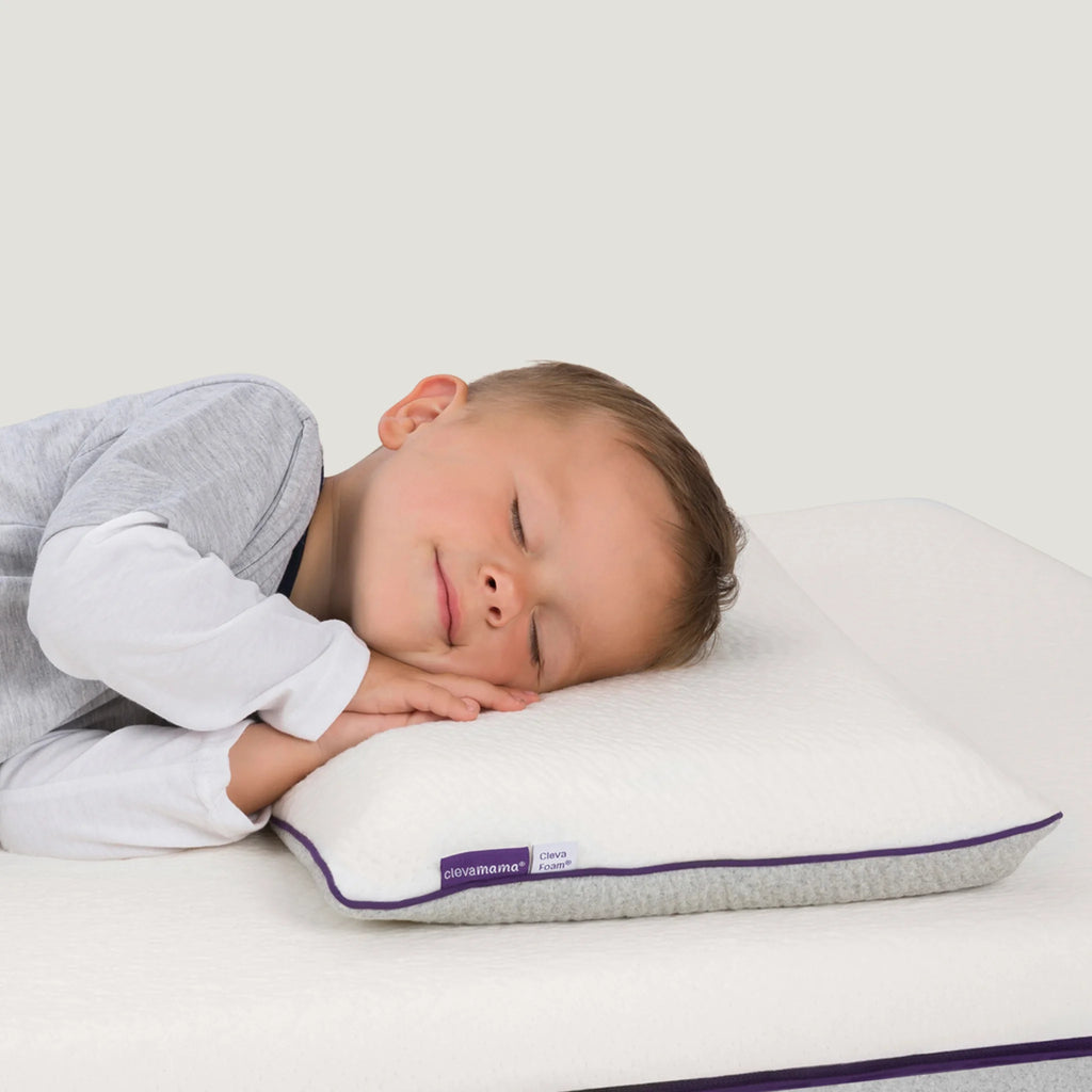 Child sleeping on a pillow with a visible brand label against a white background