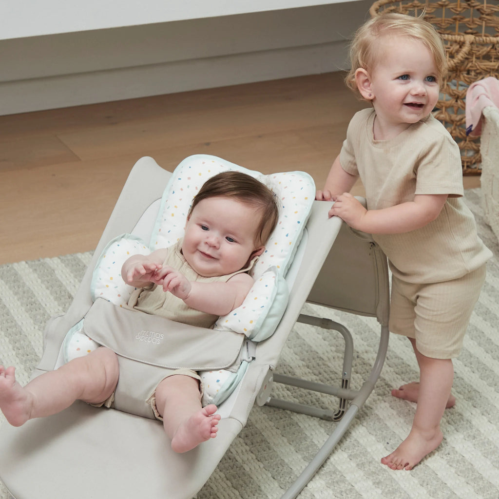 Two children in matching outfits, one baby in bouncer with head and neck support.