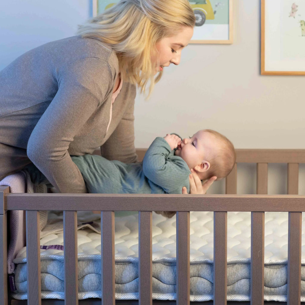 Mother placing baby on ClevaFoam Pocket Sprung Cot Mattress- breathable hypoallergenic OEKO-TEX certified infant mattress for safe and comfortable sleep.