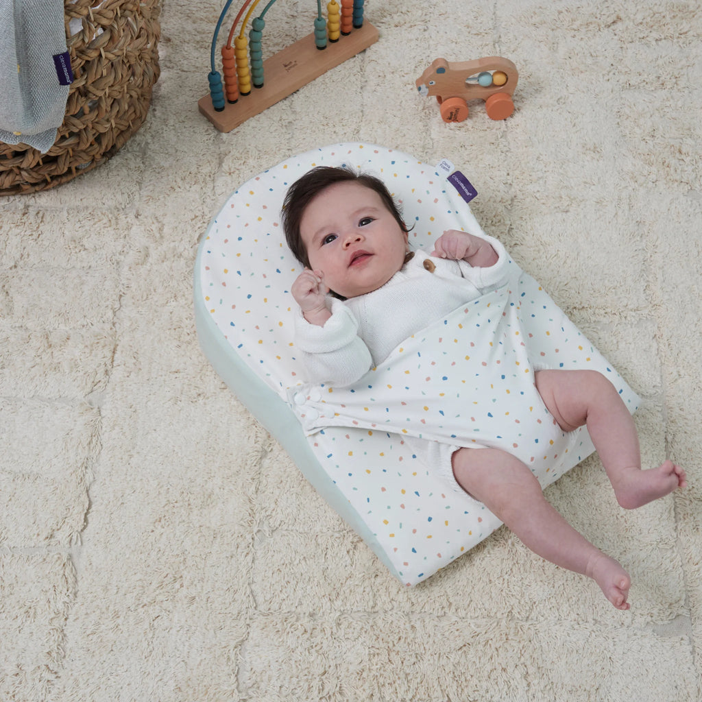 Baby lying on clevamama reflux wedge on cosy rug.